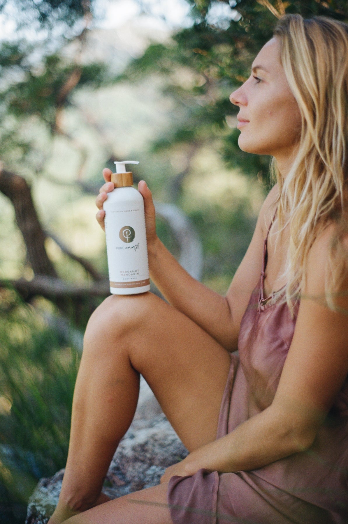 Woman sitting in forest hodling white bottle with bamboo pump label 'pure earth'