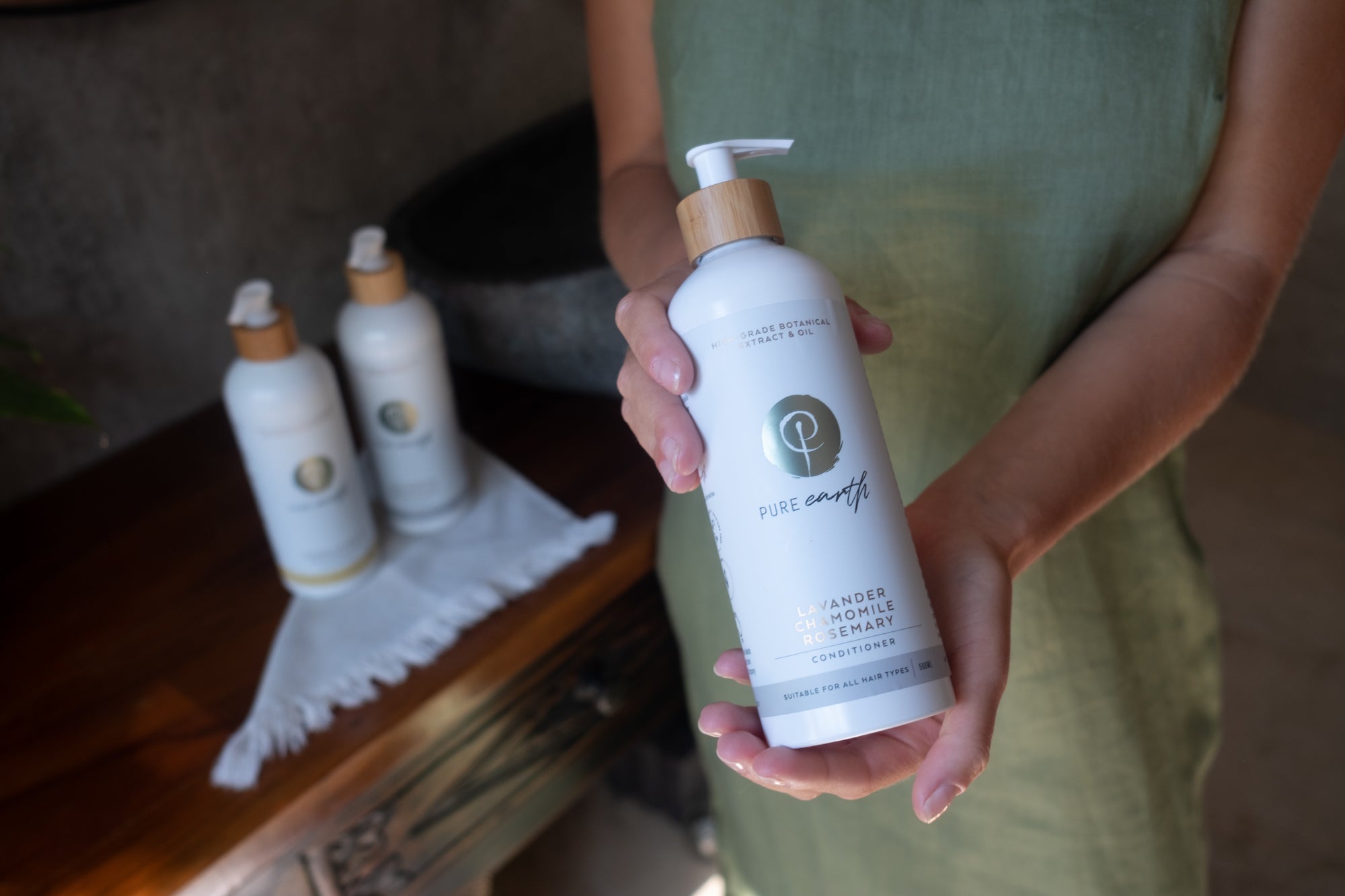 Person holding a bottle of Pure Earth hair care product with more products in the background.