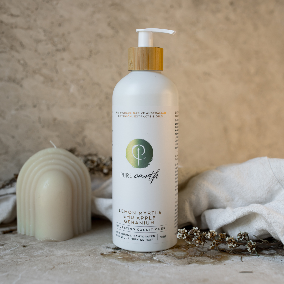 A bottle of natural conditioner with a pump dispenser, placed next to a candle and some dried plants, on a textured background.