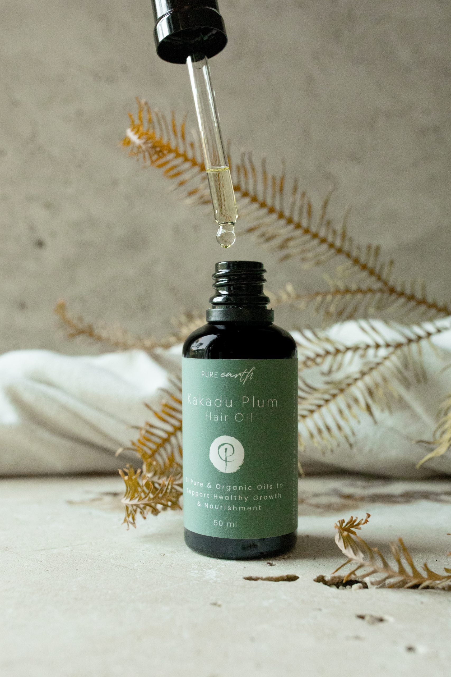Image of Pure Earth Black dropper bottle kakadu plum organic hair oil on textured surface