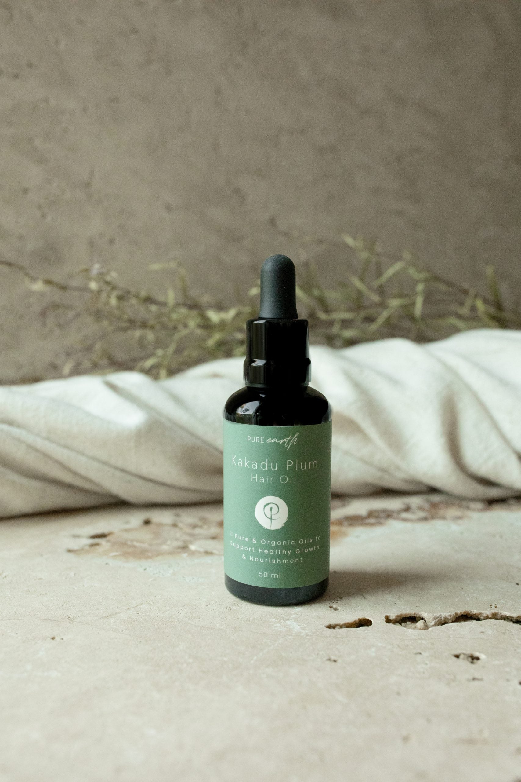 Image of pure kakadu plum hair oil with black dropper bottle and green label on textured background and with towel