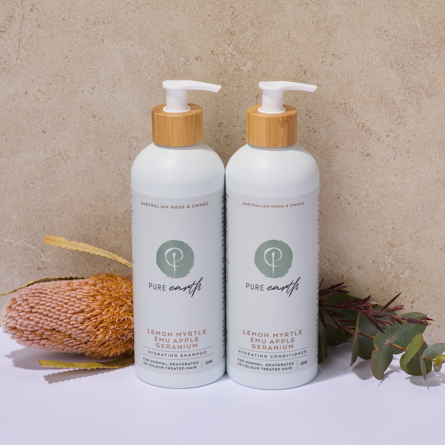 Two bottles of Pure Earth lemon myrtle emu apple geranium product on a neutral background with natural elements.