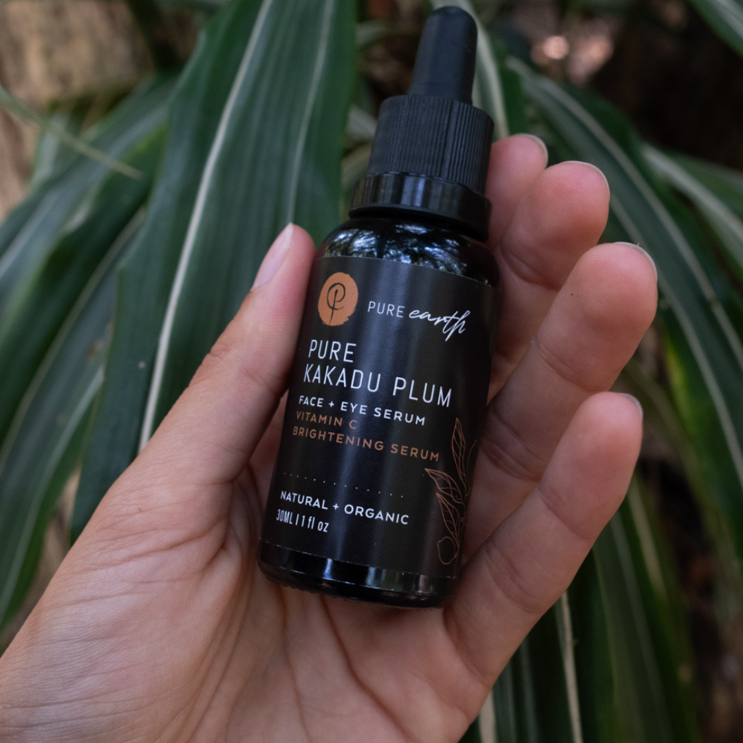 Hand holding a bottle of Pure Earth Pure Kakadu Plum Face Eye Serum against a green leafy background