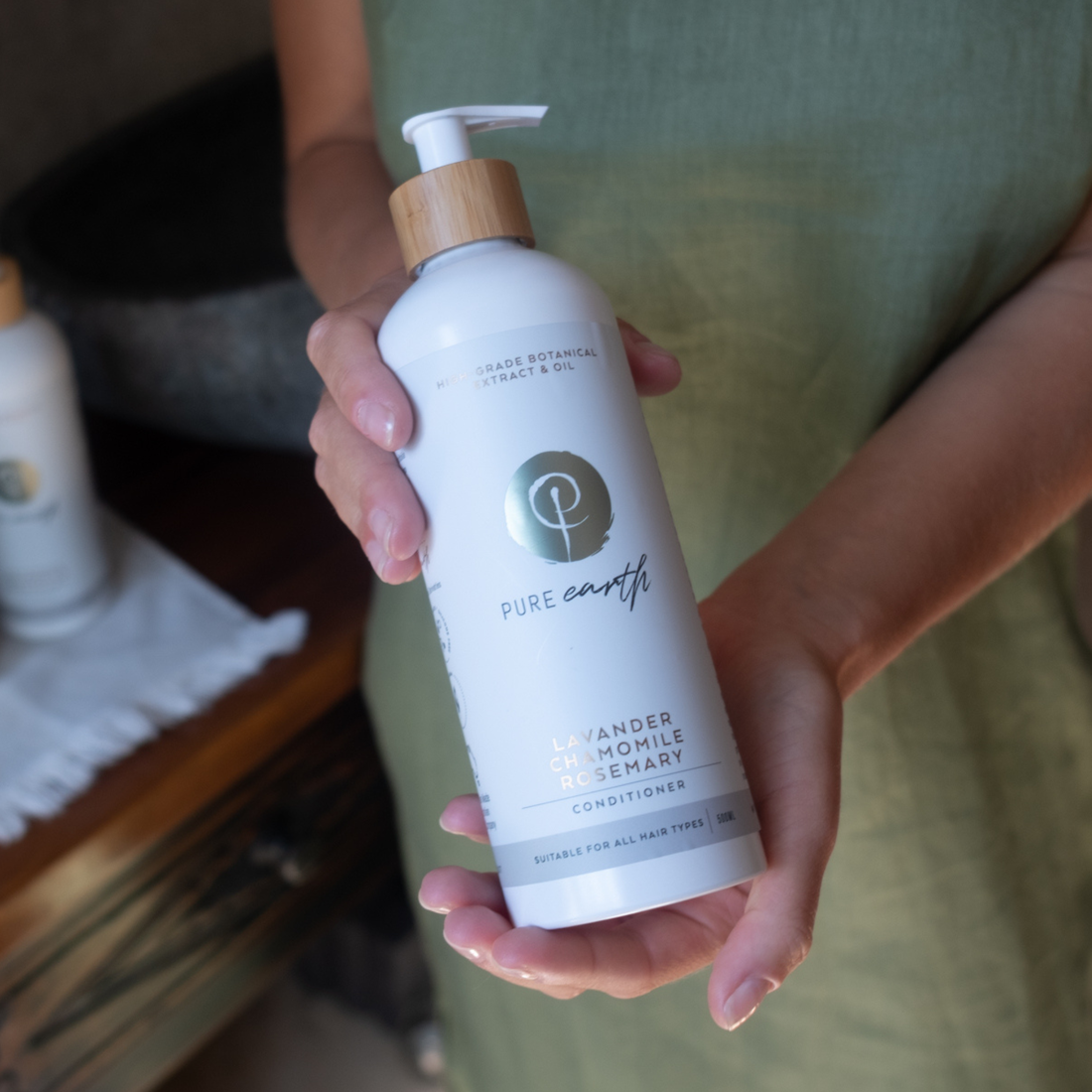 Hand holding a bottle of Pure Earth natural conditioner with a blurred background