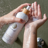 Person holding a bottle of Pure Earth natural conditioner product with a green background