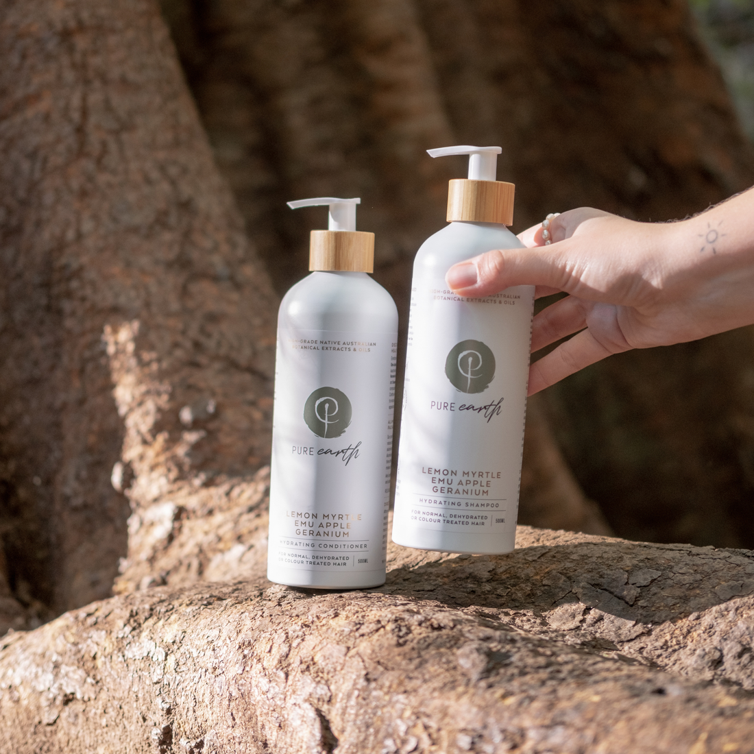 Two bottles of Pure Earth natural shampoo and conditioner products on a tree stump with a hand holding one bottle.