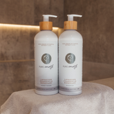 Two bottles of Pure Earth shampoo and conditioner on a towel with a blurred background tiles in a bathroom