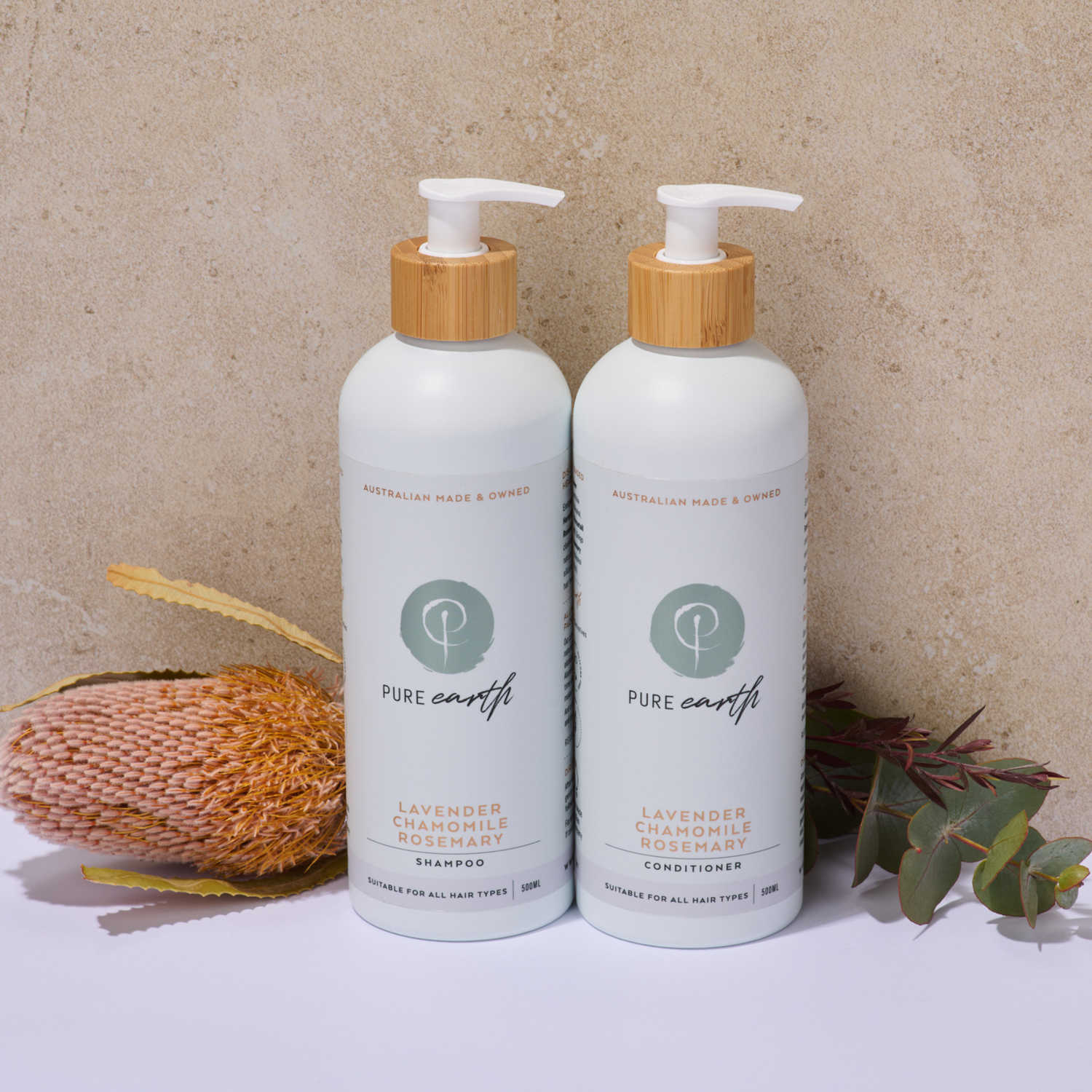 Two bottles of Pure Earth lavender chamomile shampoo and conditioner on a neutral background with natural elements and flowers.