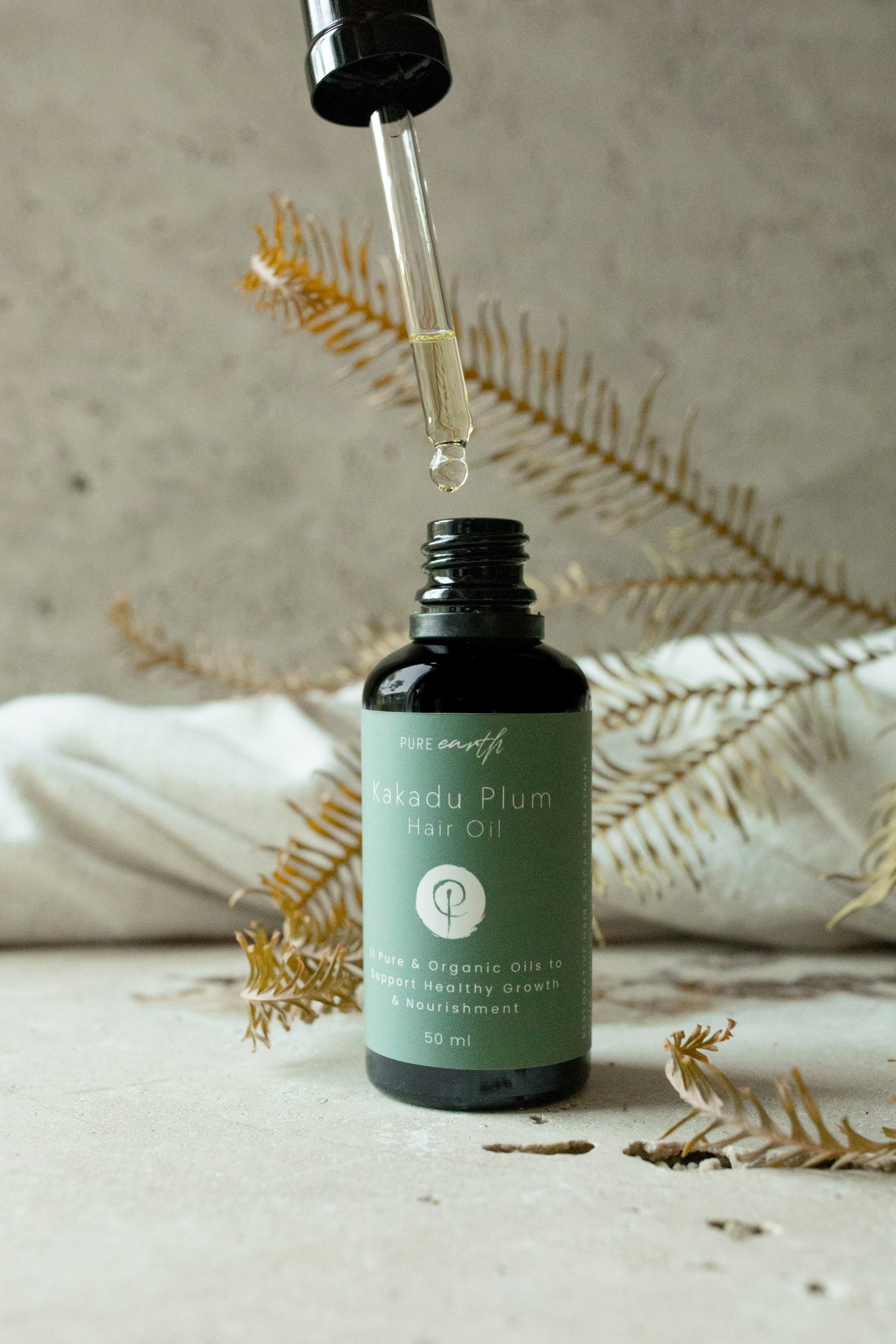 Image of Pure Earth Black dropper bottle kakadu plum organic hair oil on textured surface